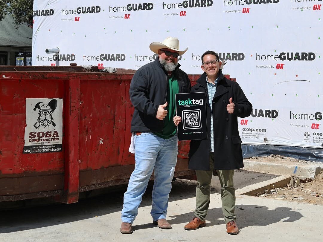 Two people standing in front of a red dumpster at an event, holding a plaque, featured image